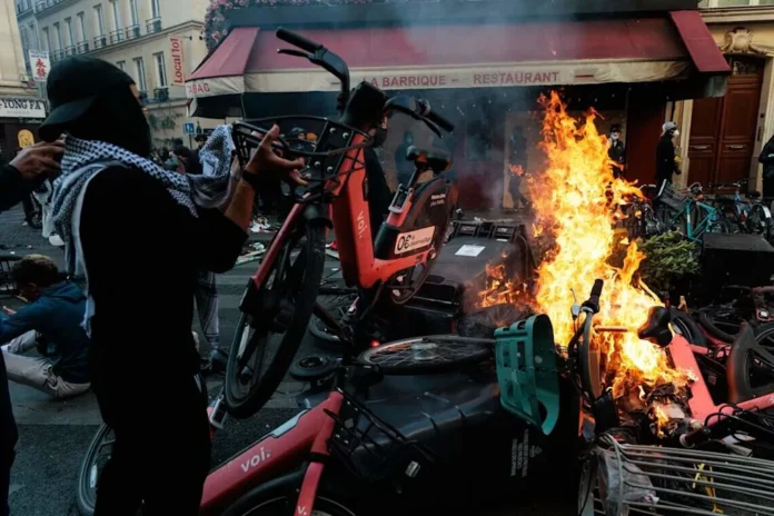 Un hombre arroja una bicicleta al fuego durante una protesta con disturbios y enfrentamientos con las fuerzas del orden cerca de la plaza de la República, en París, el 18 de octubre de 2026.